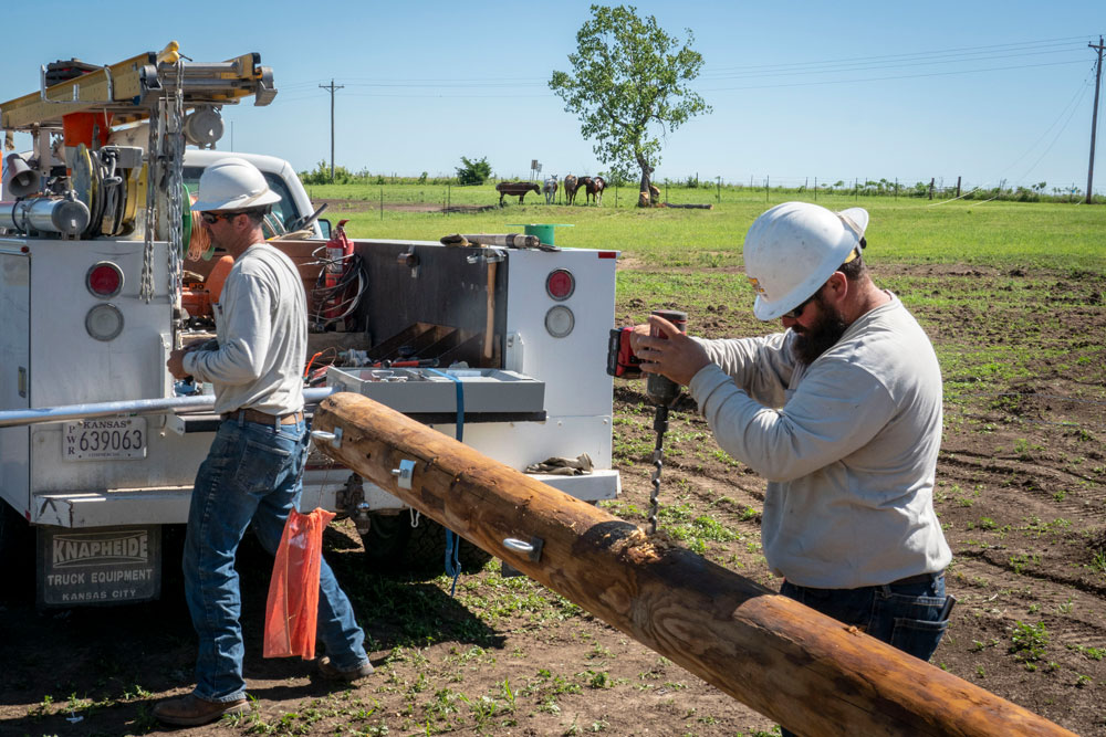 Two Bluestem Electric Cooperative linemen work on drilling holes into a power pole before it is set into the ground.