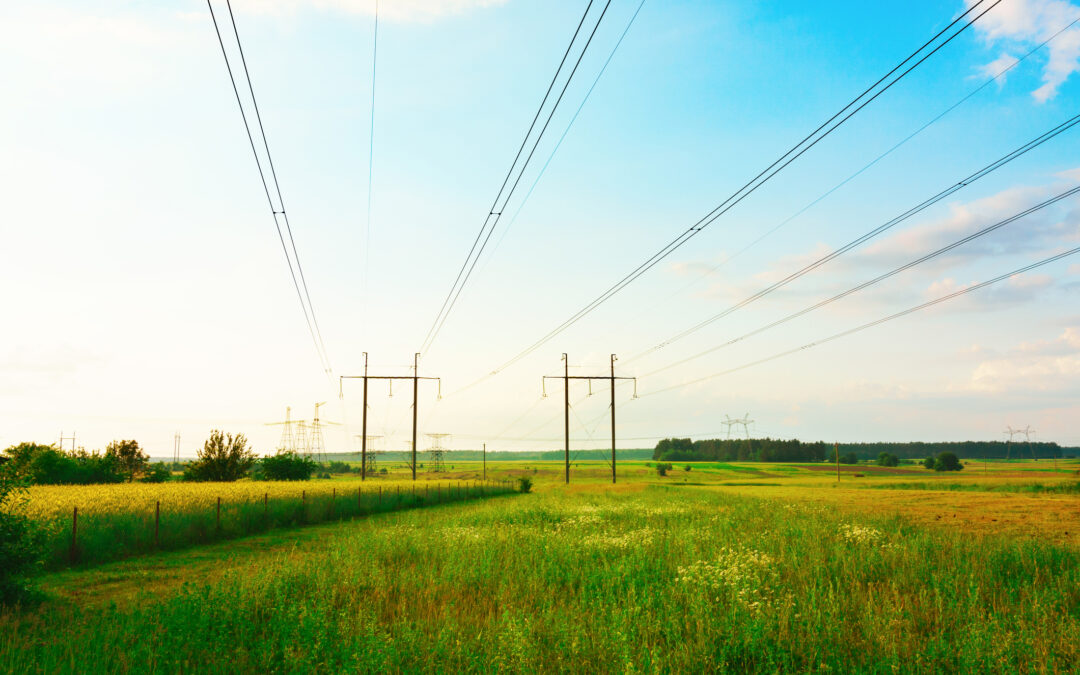 High voltage steel electricity transmission lines pylons of a power line on a green field.